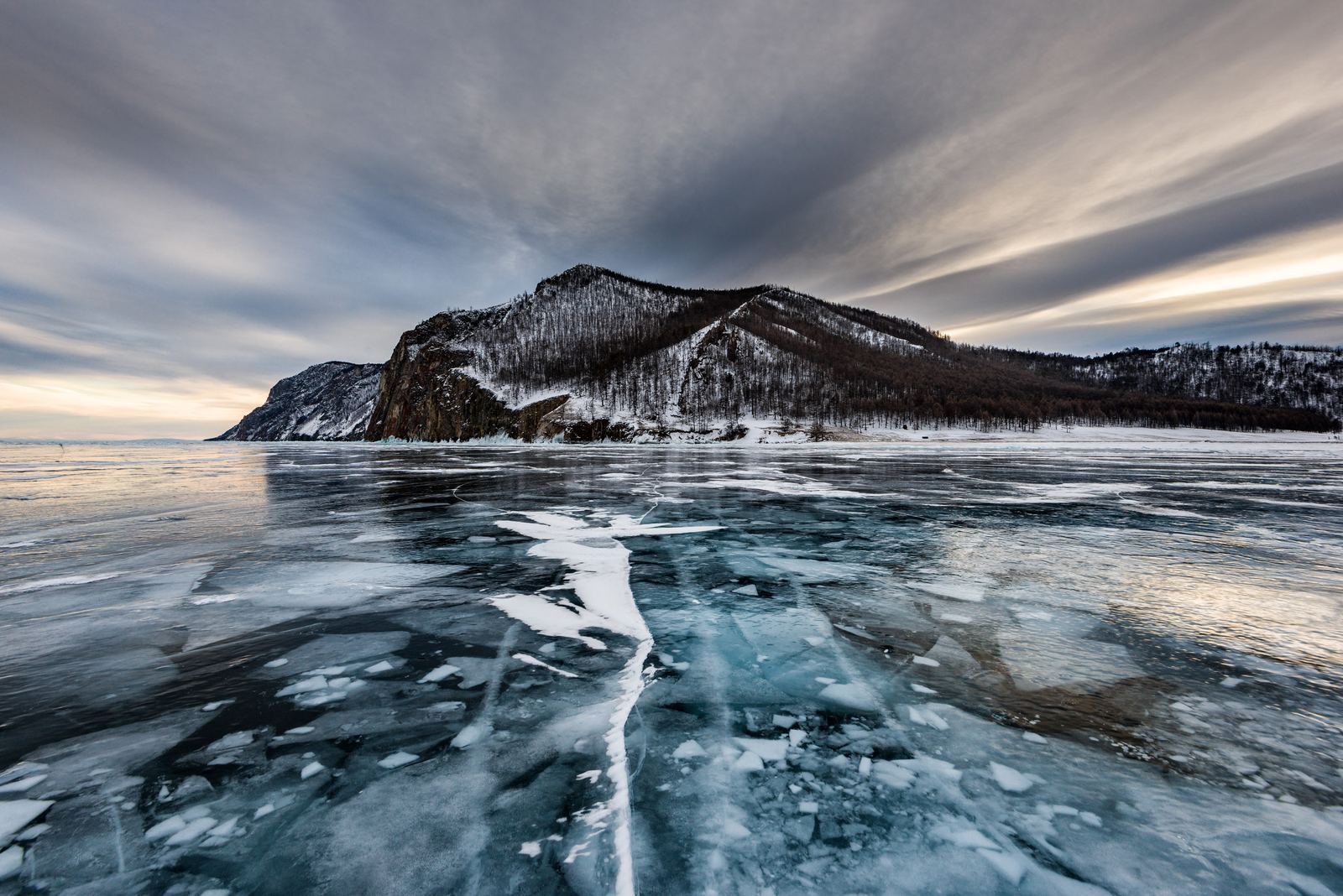 Clear blue ice and snow-dusted shore of Lake Baikal in winter