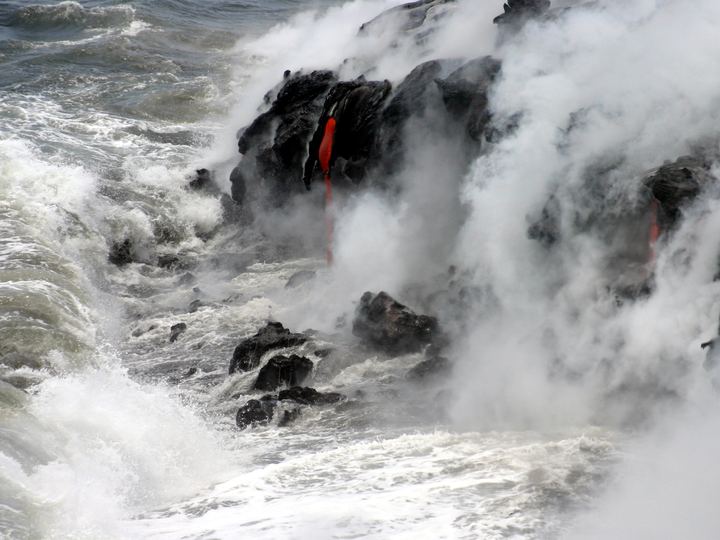 Glowing pahoehoe lava flowing into Pacific Ocean waves on Hawaii