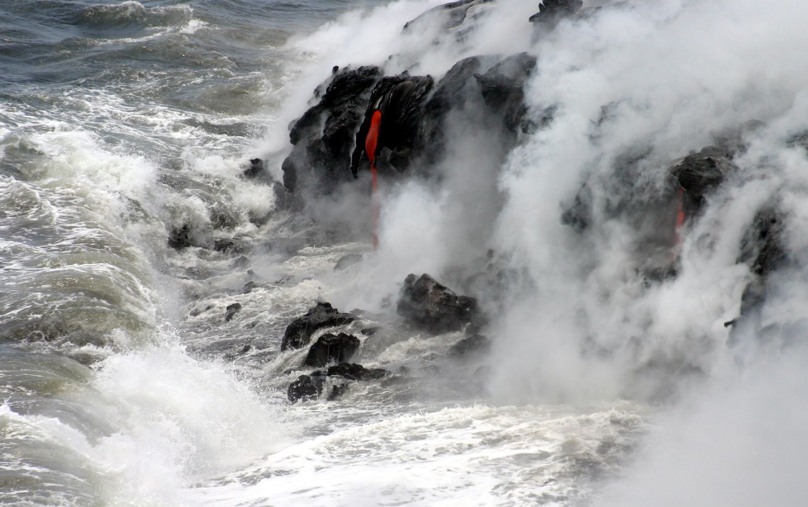 Glowing pahoehoe lava flowing into Pacific Ocean waves on Hawaii